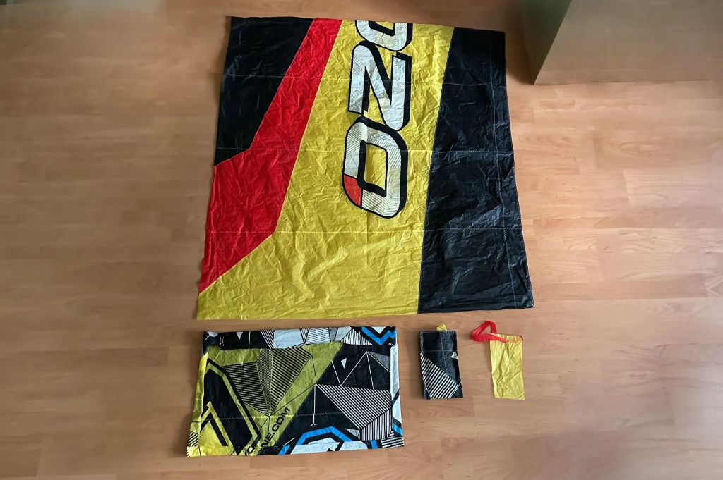 All four upcycled products laid out together, showing the beach mat, tote bag, key pouch, and canopy-strip tag.