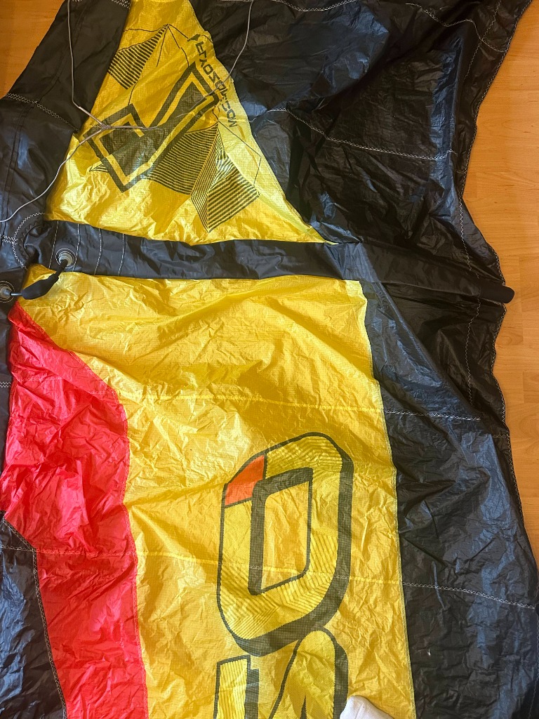 Authentic retired kitesurfing canopy laying flat, showing a bright yellow section with bold black vertical brand print, bordered by a vibrant red stripe and heavy black sail panels.