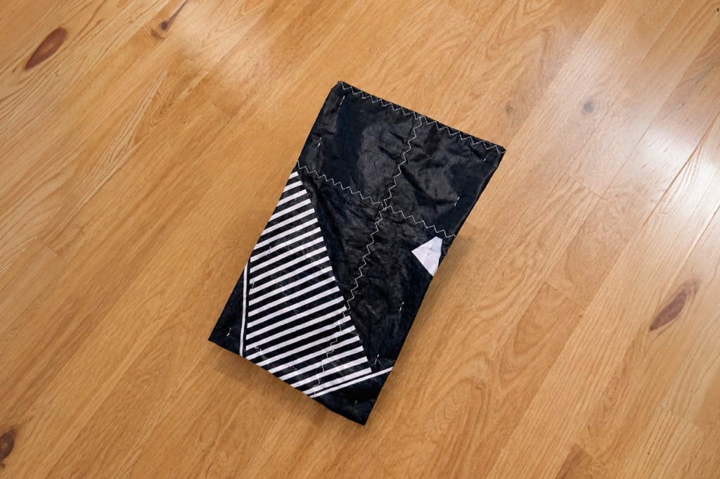 Handmade raw-cut upcycled pouch with folded flaps secured along the sides by steel staples.